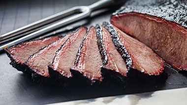a brisket cut into pieces with knife in the background