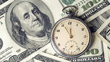 Hundred dollar bills in a pile with a clock on top